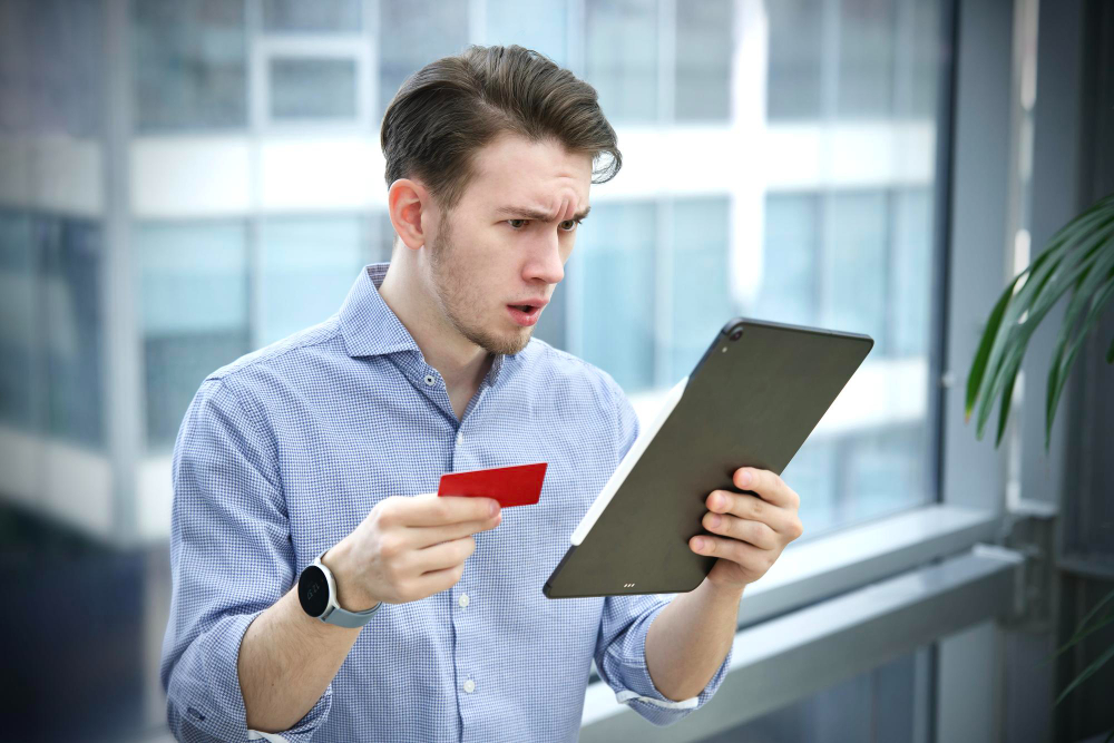 A man looking surprised while holding his credit card and a tablet
